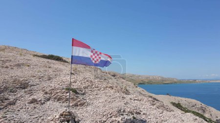 Croatian flag waiving on a sunny summer day on the top of a cliff with island archipelago. Adriatic sea on the background