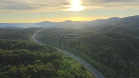 Aerial view of lonely isolated Highway Road Through Green Forest with no traffic car at sunrise dramatic and colorful sky. Drone cinematic footage