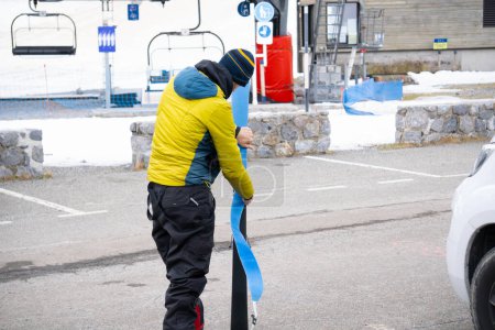 Téléchargez les photos : Homme mettre de la peau de phoque sur les skis dans le parking, à côté du camping-car, téléski en arrière-plan. - en image libre de droit