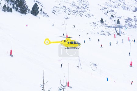 Foto de Helicóptero de rescate amarillo vuela sobre la pista de esquí con los esquiadores. fotografía en Candanchu pyrenees españa. tours en helicóptero - Imagen libre de derechos