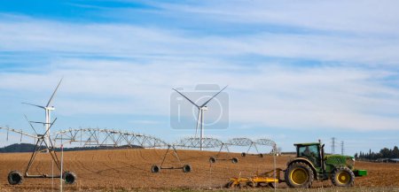 Innovative Agriculture: Green Tractor in Cultivated Field with Wind Turbines.