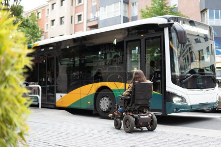 Invaliditätssammlung. Frau im Elektro-Rollstuhl vor einem für Menschen mit eingeschränkter Mobilität unzugänglichen Bus.