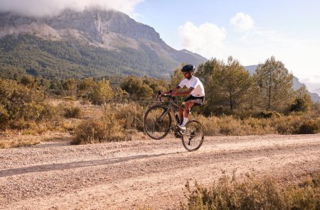 Photo for Man cyclist on gravel bicycle riding wheelie on a rear wheel.Cyclist practicing on gravel road.Gravel biking. Extreme sports and activity concept.Spain - Royalty Free Image