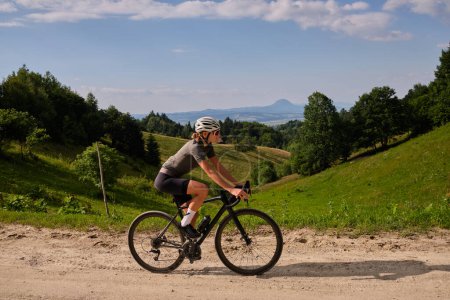 Photo for Female cyclist riding a gravel bike on a gravel road with a view of the mountains. Athlete is wearing cycling kit. - Royalty Free Image