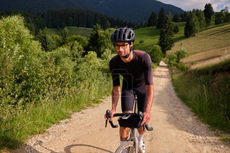Foto de Hombre ciclista con kit de ciclismo y casco de montar bicicleta de grava en la carretera de grava en las montañas con vista panorámica. - Imagen libre de derechos