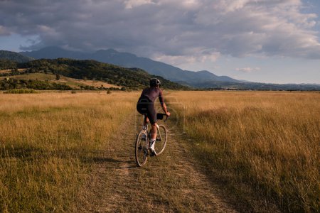 Photo for Male cyclist wearing cycling kit and helmet riding on the road a gravel bike at sunset.Sports motivation image. - Royalty Free Image