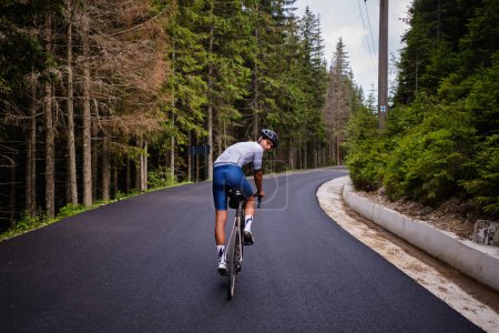 Foto de Un ciclista masculino profesional está montando una bicicleta en un camino forestal vacío. Ciclista con kit de ciclismo. Entrenamiento de ciclista en bicicleta de carretera. Preparación del concurso. - Imagen libre de derechos