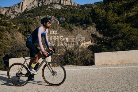 Un ciclista masculino montando cuesta arriba en una bicicleta de grava. Deportista entrenando duro en bicicleta al aire libre. Motivación deportiva. Región de Alicante en España.