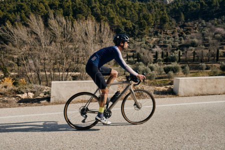 Un joven ciclista montando cuesta arriba en una bicicleta de grava.Deportista entrenando duro en bicicleta al aire libre.Motivación deportiva.Región de Alicante en España.