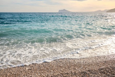 Foto de Olas de mar azules y turquesas con silueta de montaña.Paisaje marino tropical con piedras blancas y mar azul.Calp, Alicante, España - Imagen libre de derechos