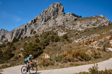 Photo for A female cyclist climbing a mountain road on a gravel bike, wearing a cycling kit and helmet.The cyclist riding between mountains, creating a beautiful and motivational image of an athlete.Spain - Royalty Free Image