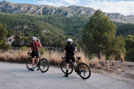 Dos ciclistas profesionales montando bicicletas de grava en una carretera de grava en un día soleado de verano. Paseo en bicicleta de grupo en el campo natural. Ventaja de grava. Aventura en bicicleta de grava. Alicante, España .
