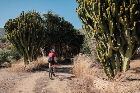 Woman cyclist is riding along a scenic mountain gravel route. Cyclist is practicing on gravel road. Beautiful sunny day for cycling. Alicante region, Spain.
