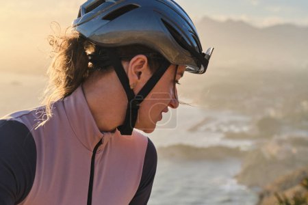 Close up portrait of a female cyclist during sunset. Beautiful woman cyclist wearing cycling kit, sunglasses and helmet. Sport equipment. Sports portrait. Training outdoor
