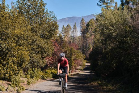 A female cyclist is riding along a scenic mountain gravel route in a forest on Tenerife Island. Cyclist is practicing on gravel road. Beautiful sunny day for cycling. Spain.