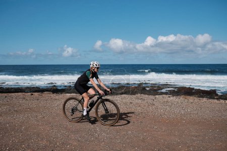 Radfahrerin auf einem Schotterweg mit schöner Aussicht auf den Atlantik auf Teneriffa, Kanarische Inseln, Spanien. Sportliche Motivation. Radtraining im Freien in Spanien. Abenteuer Radfahren.