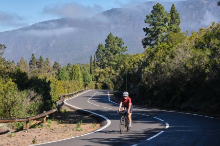 A female cyclist riding a bicycle on the road. Attacking the climb. Effortful cycling mood. Cycle in beautiful nature. Woman cyclist wearing cycling kit and helmet. Tenerife, Canary Island, Spain.