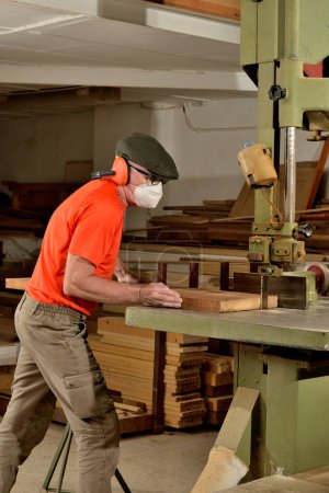 Photo for Carpenter operator working wood on band saw with mask and ear protection - Royalty Free Image