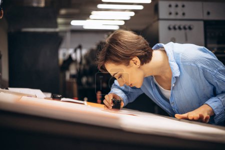 Téléchargez les photos : Femme typographe travaillant dans une imprimerie avec papier et loupe - en image libre de droit