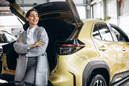 Photo for Young woman sitting on the trunk of a car in a car showroom - Royalty Free Image
