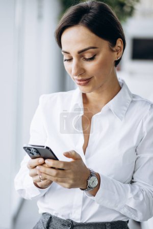 Téléchargez les photos : Femme d'affaires utilisant le téléphone près du bureau de la fenêtre - en image libre de droit