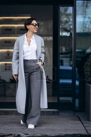 Foto de Hermosa mujer de negocios en abrigo gris fuera del edificio de oficinas - Imagen libre de derechos