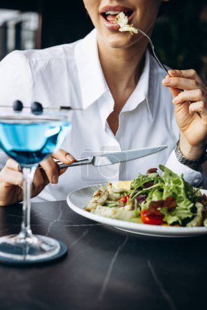 Téléchargez les photos : Femme buvant du coctail et mangeant de la salade dans un café - en image libre de droit