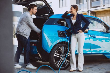 Photo for Couple talking by their electric car while its charging - Royalty Free Image