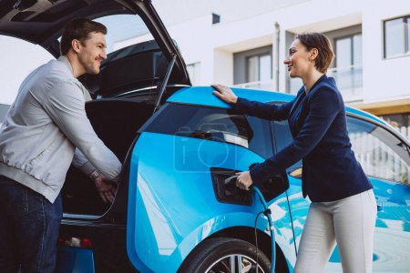 Photo for Couple talking by their electric car while its charging - Royalty Free Image