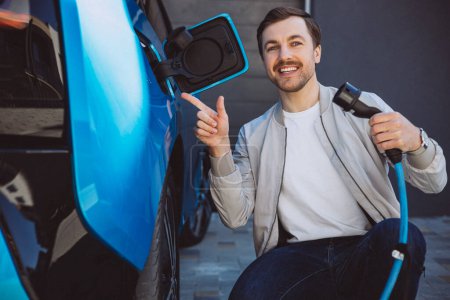 Photo for Man holding charger from his electric car - Royalty Free Image