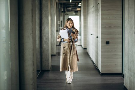 Foto de Mujer de negocios sosteniendo carpetas y usando el teléfono y caminando en la oficina - Imagen libre de derechos