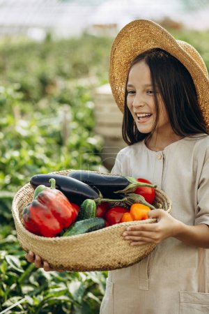 Téléchargez les photos : Jeune fille avec panier plein de légumes debout dans la serre - en image libre de droit