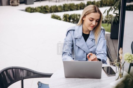 Téléchargez les photos : Femme assise dans un café travaillant sur un ordinateur portable et buvant du café - en image libre de droit