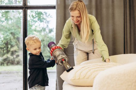 Photo for Mother with her son vacuuming sofa at home - Royalty Free Image