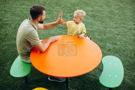 Téléchargez les photos : Père avec son fils assis à la table applaudissements mains - en image libre de droit