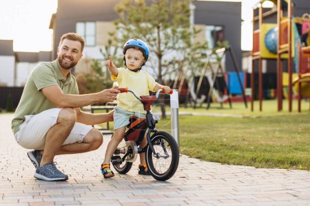 Téléchargez les photos : Père apprenant à son petit fils à faire du vélo - en image libre de droit