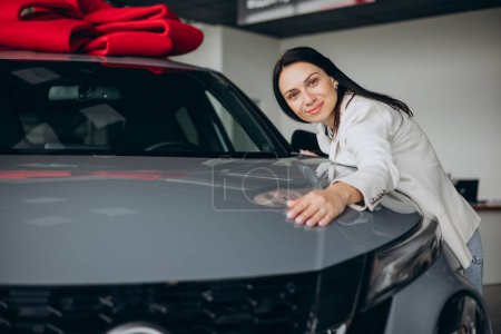 Téléchargez les photos : Femme étreignant une nouvelle voiture dans une salle d'exposition de voiture - en image libre de droit