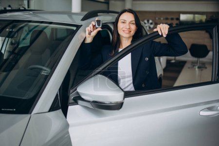 Photo for Sales woman in car showroom holding car keys and standing by the car - Royalty Free Image