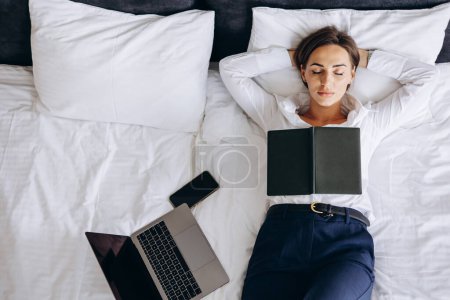 Téléchargez les photos : Femme d'affaires dormant dans une chambre d'hôtel avec ordinateur portable et téléphone couché sur le lit - en image libre de droit