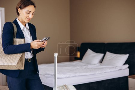 Photo for Business woman in a hotel room talking on the phone and carrying baggage - Royalty Free Image