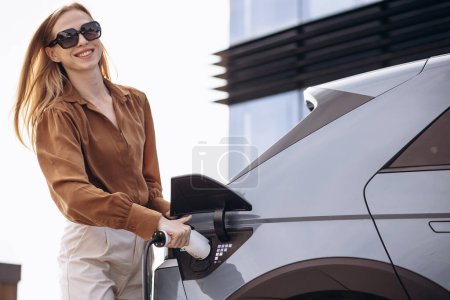 Photo for Woman puts charging cable into electric car - Royalty Free Image