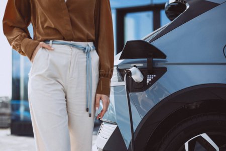 Photo for Electric car charging on the background and woman standing in front - Royalty Free Image