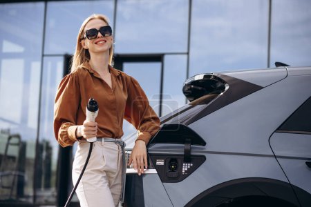 Photo for Woman puts charging cable into electric car - Royalty Free Image