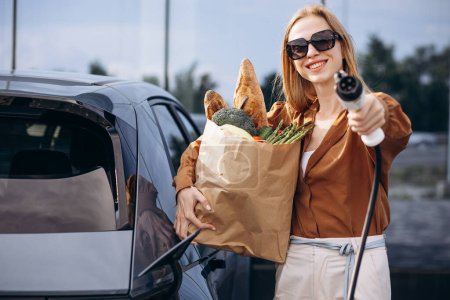 Photo for Woman doing grocery shopping while electric car charging - Royalty Free Image