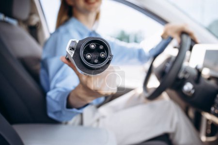 Téléchargez les photos : Femme assise dans la voiture et tenant le câble de charge - en image libre de droit