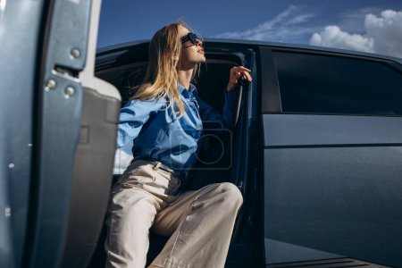 Téléchargez les photos : Femme assise à l'intérieur de sa voiture électrique avec porte ouverte - en image libre de droit