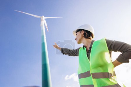 Téléchargez les photos : Femme ingénieur avec casque debout près des éoliennes - en image libre de droit