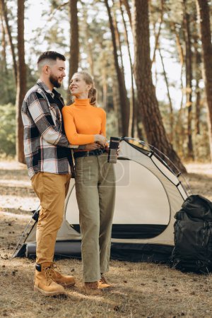 Téléchargez les photos : Voyageurs en couple dans la forêt près de leur tente buvant du thé chaud - en image libre de droit