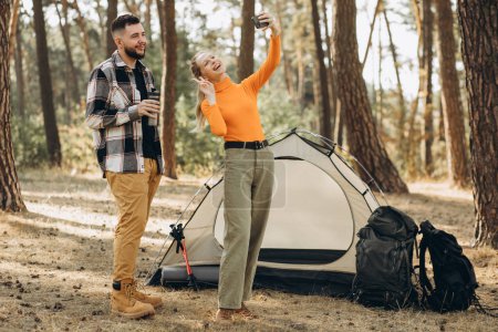 Téléchargez les photos : Couple faisant des photos dans la forêt près de leur tente - en image libre de droit