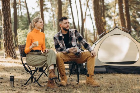 Photo for Couple drinking tea by their tent in forest - Royalty Free Image